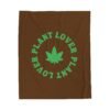 This plant lover weed leaf blanket features a bold weed leaf design with 'Plant Lover' written around it, all in a green color same as the weed leaf itself. Weed Leaf blanket is brown